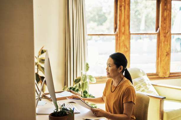 istock Senior Asian woman using a computer to write a book or a document. Old female working from home on a PC browsing the internet. Mature lady concentrating on a screen scrolling on the internet 1407659434