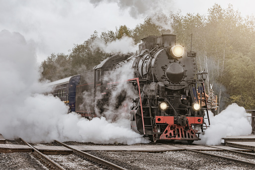 Retro steam train departs from the station wooden platform at cloudy autumn evening.