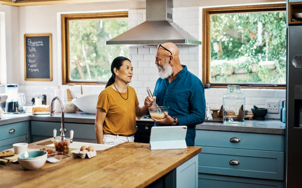 hombre y mujer felices uniéndose mientras preparan el almuerzo. pareja interracial senior cocinando con una tableta digital juntos en la cocina de casa. marido y mujer jubilados preparando comida con una receta en línea. - cooking senior adult healthy lifestyle couple fotografías e imágenes de stock