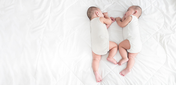 Adorable five months old baby boy twins on the bed, Twin infants sleep on the white soft blanket in the bedroom