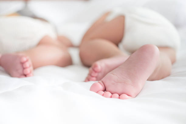 de perto pés de recém-nascidos na cama, bebês gêmeos deitam em cobertor branco macio, conceito de infância feliz - multiple birth - fotografias e filmes do acervo