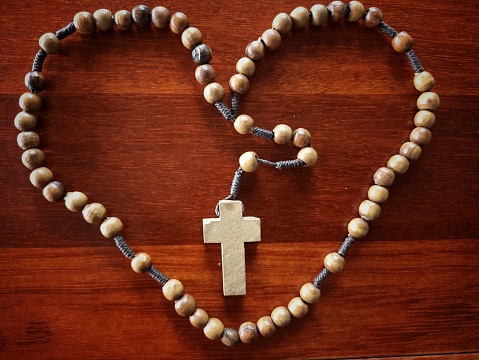 Wooden rosary in love or heart shape on brown wood table background. Praying rosary concept. Catholic symbol of faith.