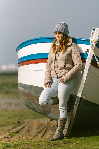 Vertical photo of a woman leaning on the bow of a fishing boat at low tide