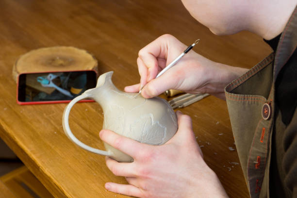 istock Online pottery course. Distance education. E-learning concept. Potter carving ornament on jug watching video on phone 1407668483