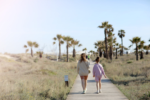 Summer holiday vacation on beach at sea. mom with child girl are walking on wooden walkway between palm trees on sunny day. High quality photo.