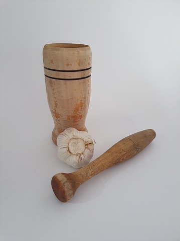 Close-up of wooden mortar or pestle with a garlic bulb on white background.