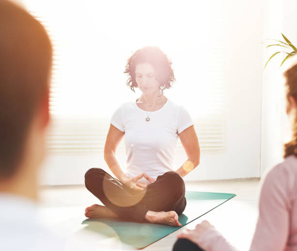 istock Yoga instructor training people during a fitness class in a studio. Female yogi teaching breathing techniques with mindful meditation exercises for zen energy in lotus pose during a lesson indoors 1407682779
