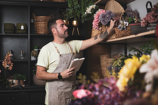 a florist browsing the shelves of his store to take inventory while writing down any missing stock in his notebook.own business