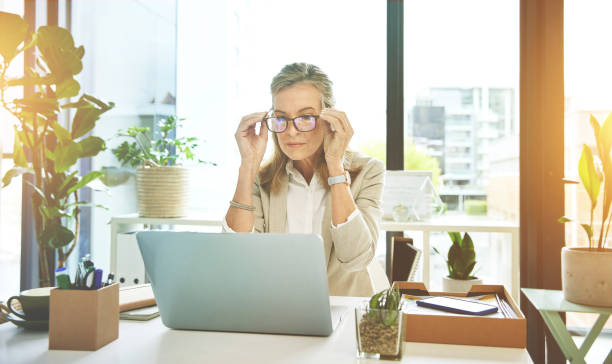 istock Female boss networking with clients on the web. Manager adjusting spectacles while reading and sending emails. Mature business woman using laptop browsing online putting on her glasses at work. 1407684365