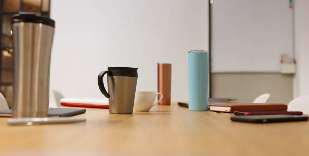 sustainable products in office Travel mug on conference table in empty board room at workplace -using sustainable products in office settings bottled water on table stock pictures, royalty-free photos & images