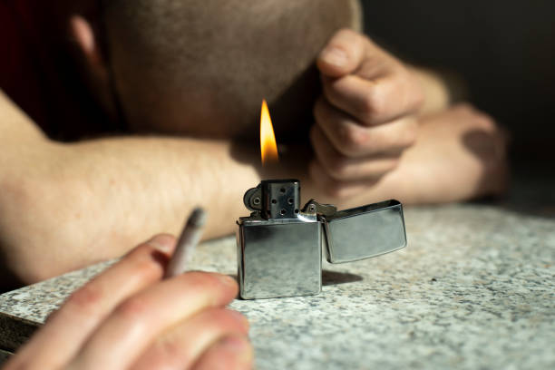 istock Gasoline lighter burns on table. Fire in background of sleeping guy. Party details. 1407686688