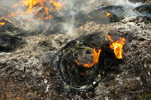 Burning wheels in landfill. Details of fire. Ashes and smoke. Destruction of ecology.