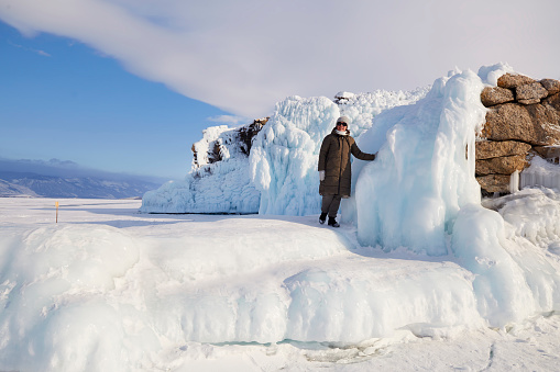 A happy woman stands on a rock covered with snow and icicles. Winter trip on the frozen lake Baikal.