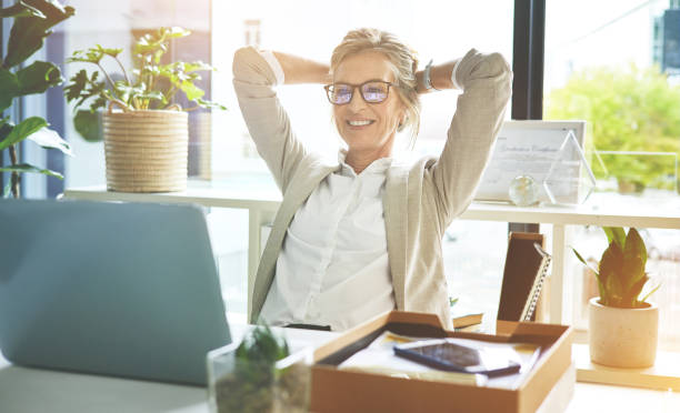 행복한 성숙한 관리자는 마감일과 업무로 만족하고 안심했습니다. 성취감을 느끼고 사무실에서 머리 뒤에 손으로 스트레칭하는 편안한 휴식을 즐기는 비즈니스 여성. - business women computer cheerful 뉴스 사진 이미지