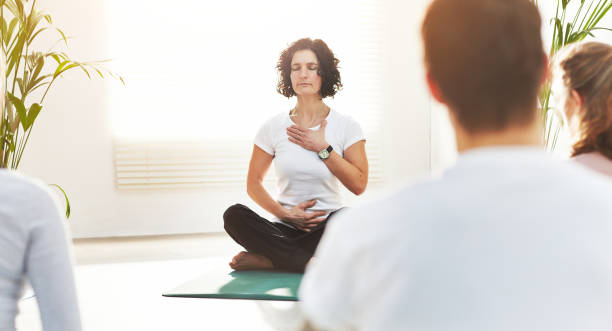Yoga instructor training people in a fitness class in studio. Yogi teaching pranayama breathing techniques with hands on chest and belly. Practicing mindful meditation for zen energy in lotus pose instructor de yoga entrenando a las personas en una clase de fitness en el estudio. yogui enseñando técnicas de respiración pranayama con las manos en el pecho y el vientre. practicar la meditación consciente para la energía zen en la postura del loto