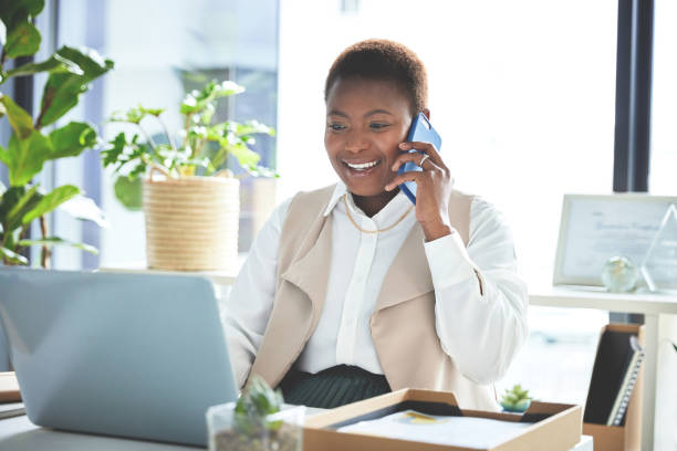istock Businesswoman chatting via phone and using a laptop in modern office space. Multitasking african american female employee having a business call and typing a quote for a client while sitting at work 1407696630