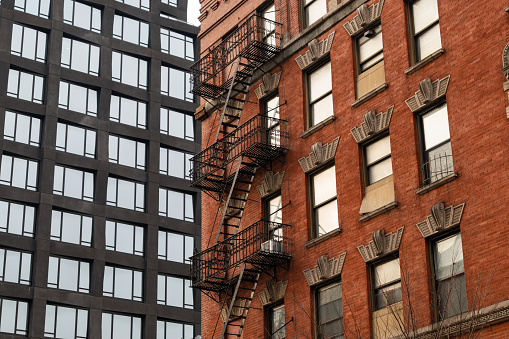 Looking up at an old brick building with fire escapes next to a modern residential skyscraper in Tribeca of New York City