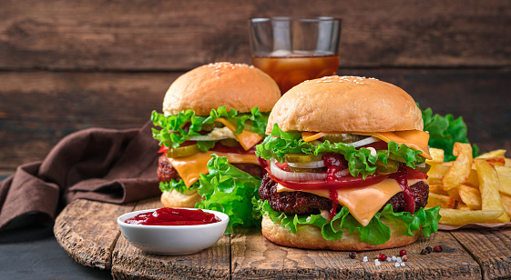 Two juicy burgers, French fries and colla on a wooden background. Fast food.