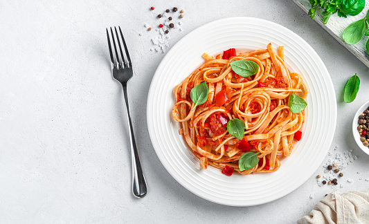 Classic linguini pasta with tomatoes on a light gray background. Top view, space to copy.