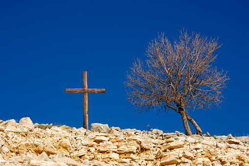 Wooden cross on rocky landscape over sunny blue sky