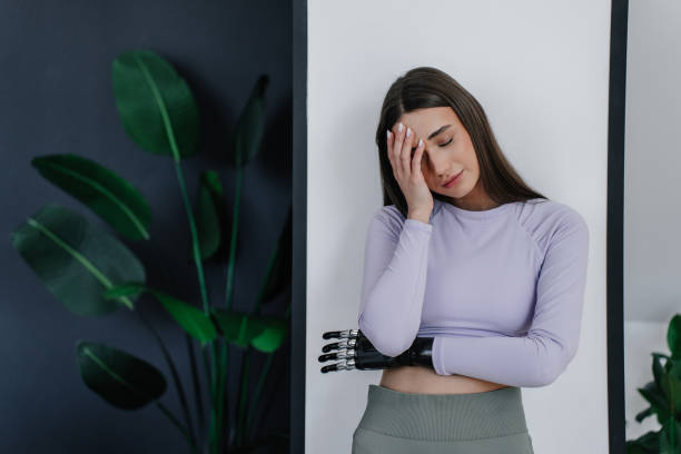 istock Exhausted beautiful disabled young woman with  bionic hand prosthesis after workout touching head eyes closed, tired. Attractive disabled girl with headache, sleepy at home. Medicine and electronics. 1407718583