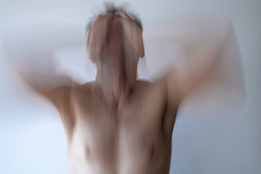 Creative photo of a man with a naked torso expressing madness, stress or anguish. Photo shot with slow shutter technique to convey that concept.