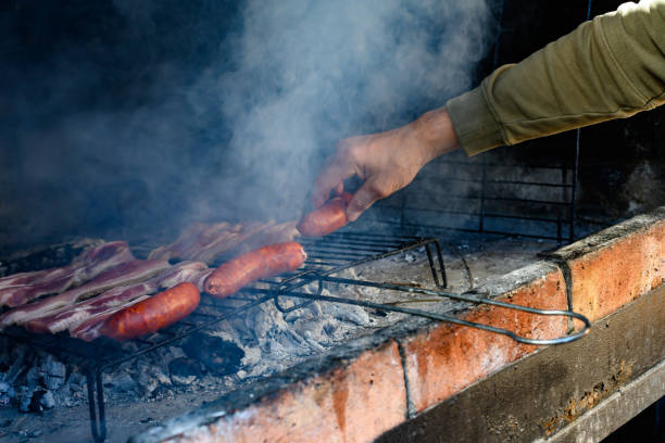 istock Man's hand puts sausages and pork belly on barbecue coals 1407721332