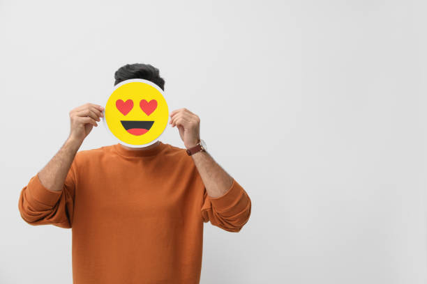 Man hiding emotions using card with drawn smiling face on white background