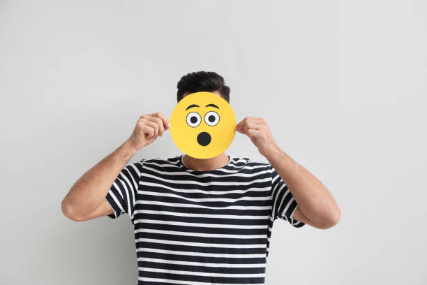 istock Man hiding emotions using card with drawn surprised face on white background 1407722196