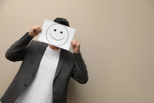 istock Man hiding emotions using card with drawn smiling face on beige background. Space for text 1407722315
