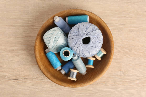 istock Color sewing threads in bowl on wooden table, top view 1407723723