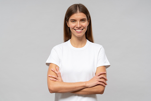 Portrait of cheerful young woman standing with arms crossed and smiling isolated on gray background