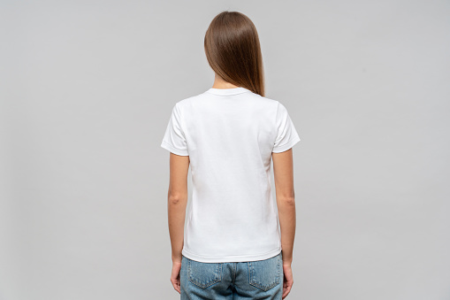 Back view of woman standing in white t-shirt, isolated on gray background, template or mockup for logo