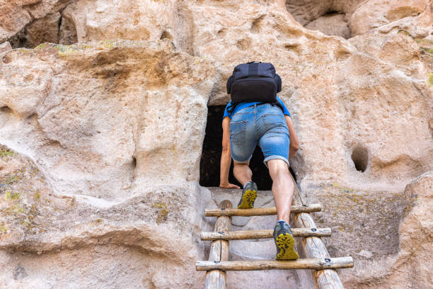 homme grimpant �à l’échelle sur le sentier main loop randonnée au monument national de bandelier au nouveau-mexique, états-unis pendant l’été sur la falaise à l’habitation troglodyte utilisée par les autochtones - ancient pueblo peoples photos et images de collection