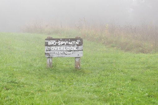 Big Spy Mountain overlook trail sign entrance with famous view in mist fog weather on Blue Ridge Parkway, Virginia national park in fall season and green grass