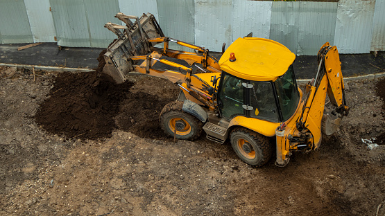 yellow construction excavator throws the earth onto a flower bed, an unusual angle