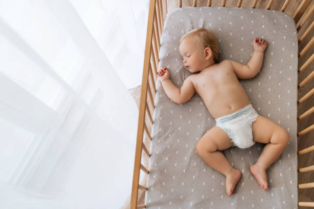 Upper view copy space portrait of cute baby sleeping in his bed lying on back watching sweet dreams Upper view copy space portrait of cute blond baby sleeping in bed on his back, feeling safe, watching sweet dreams, resting, growing, gaining strength, getting strong. Childcare concept. Nap time lying on back stock pictures, royalty-free photos & images