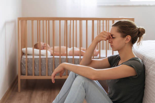 istock Side view of mother with postnatal depression symptoms sitting on floor while baby sleeping in bed 1407729525