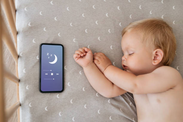 oberansicht des baby-nickerchens in seinem bett neben dem telefon, das schlaflied in der schlaf-app für baby spielt - phone cradle stock-fotos und bilder