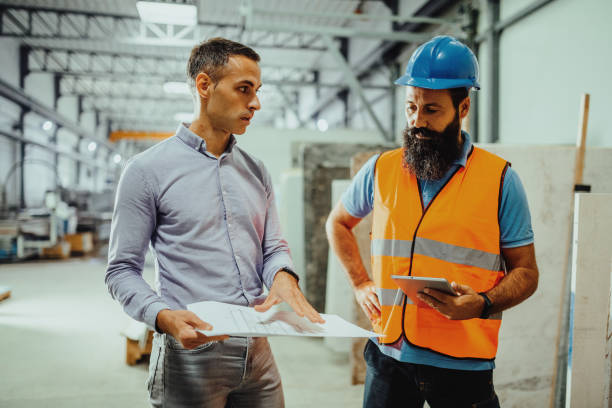 istock Employees and engineers in industry hall, discussing together blueprint 1407729602