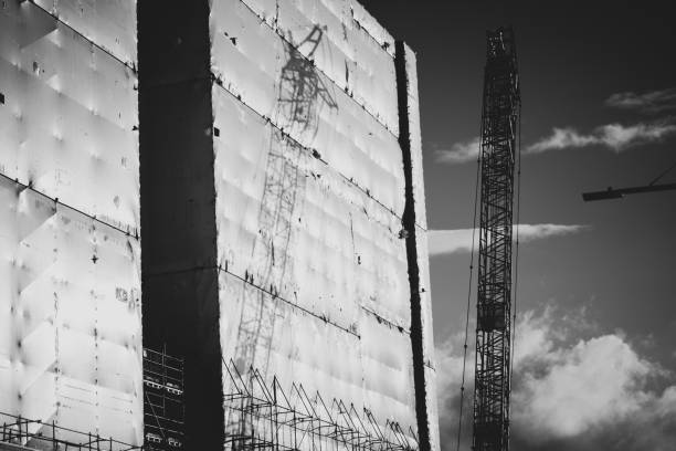istock Construction shadow, tall crane reflected on side of building wrapped in white protective plastic shrink wrap 1407729950