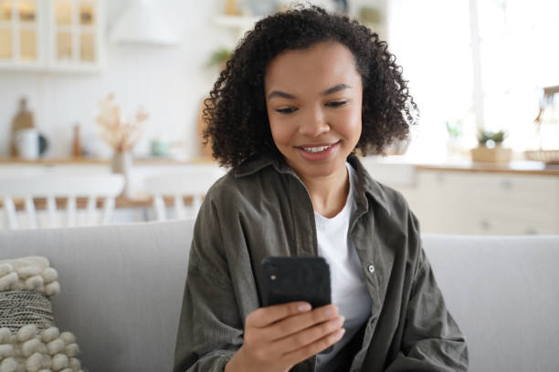 istock Young biracial girl chat or post at social network, using smartphone apps, sitting on sofa at home 1407730576