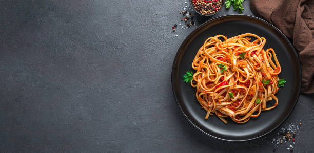 Linguini pasta with tomato sauce and parsley on a dark background.