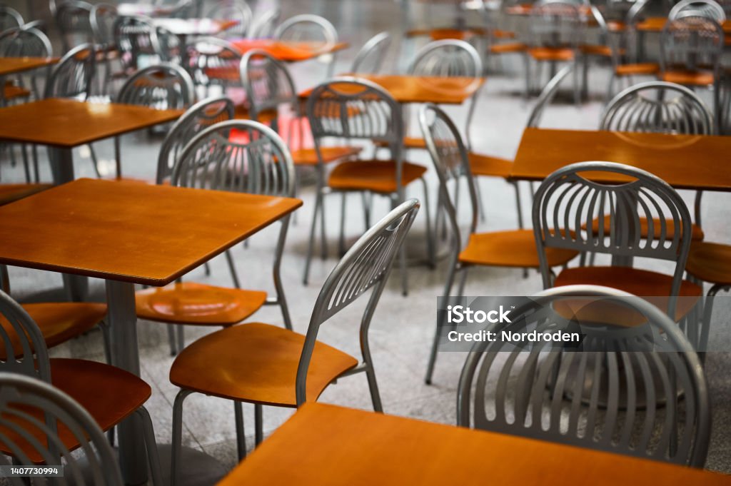 Wooden tables and chairs at large empty foodcourt in mall Group of elegant small wooden tables and chairs of restaurant at large empty foodcourt on contemporary shopping center level Cafeteria Stock Photo