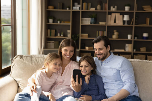 istock Family with kids relaxing on sofa having fun using smartphone 1407731098