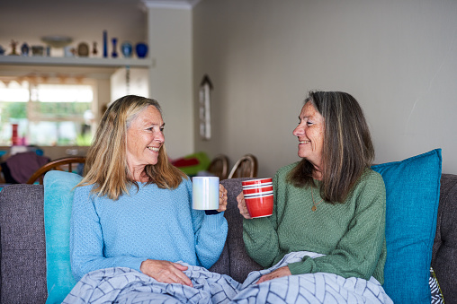 Smiling senior sisters staring at each other with a smile and sharing a cup of coffee.