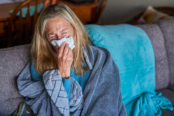 istock Sick senior woman blowing her nose on the couch 1407732015