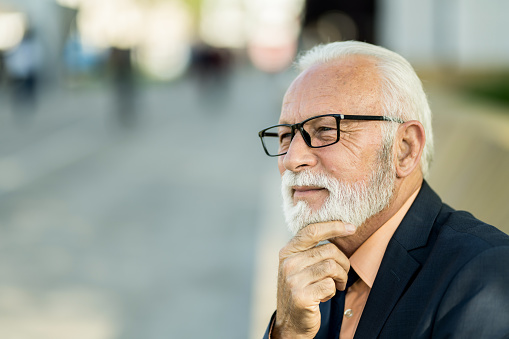 Happy senior grey haired 60s man with beard head shot. Positive retiree in glasses looking, smiling at camera, posing at home. Elderly aged customer, client, grandfather close up portrait