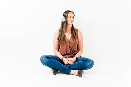 Woman sitting on ground cross legged listening to headphones looking off in distance