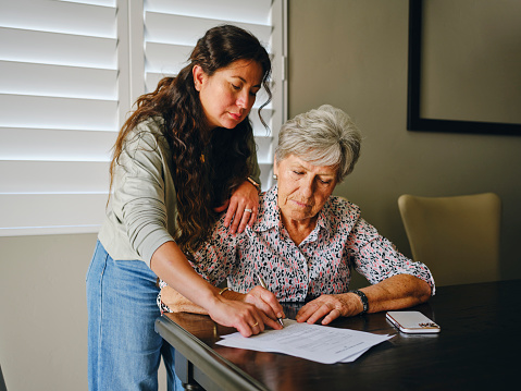 A Hispanic woman, helping a senior aged woman prepare financial documents.